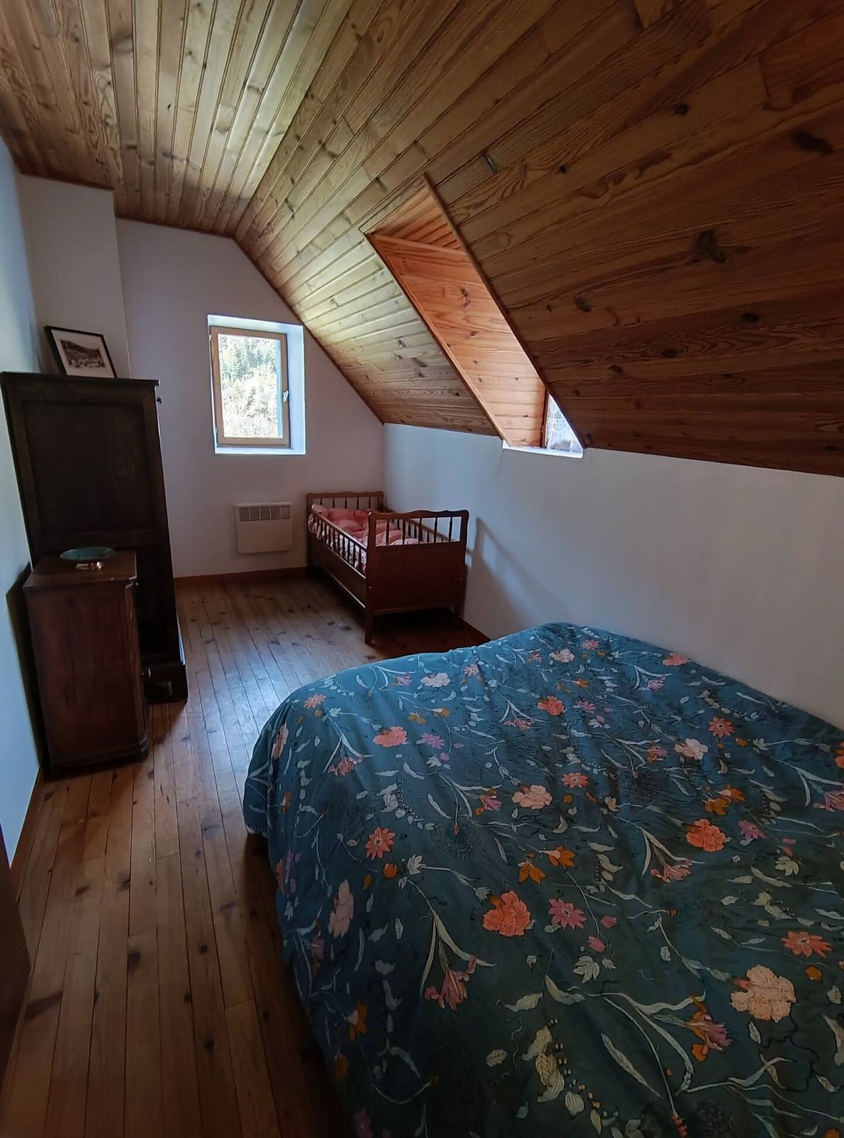 La chambre avec un grand lit fleuri et un lit bébé en bois