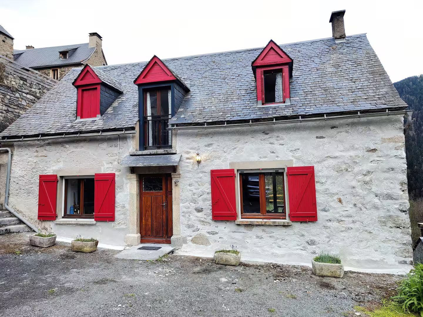 La façade en pierre de la maison, avec ses volets rouges et sa porte en bois